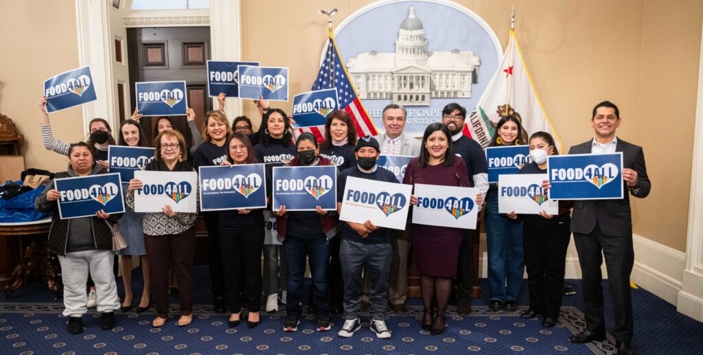 Advocates and legislators hold signs that say "Food4All."
