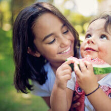 Girl is hugging her baby sister who is eating water melon